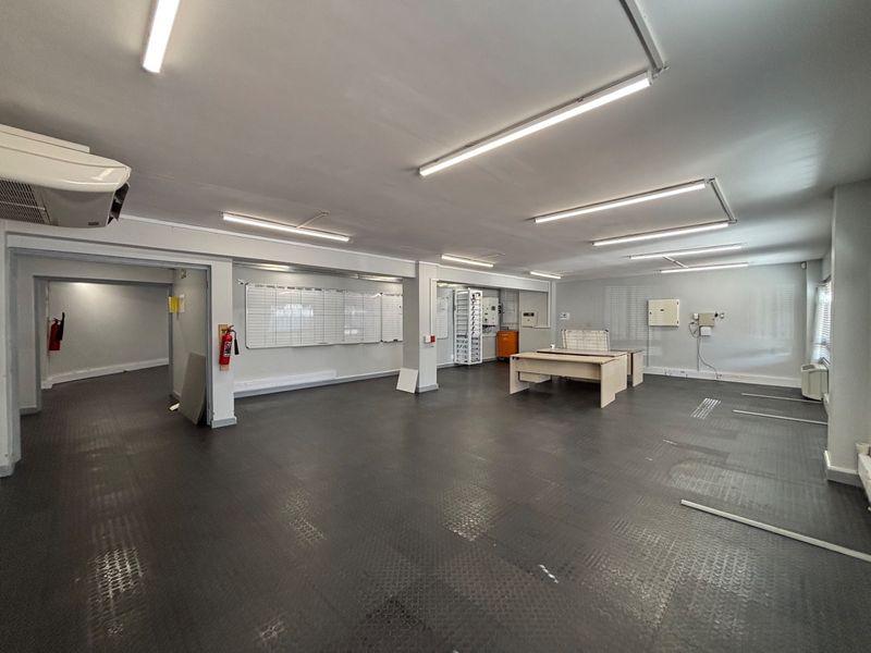 Spacious open-plan office area featuring durable rubber flooring, integrated fluorescent lighting, and wall-mounted air conditioning, suitable for a flexible workspace layout.