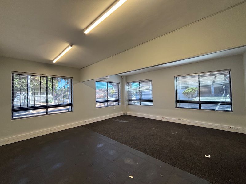 A spacious, empty office area featuring large windows with venetian blinds, fluorescent lighting, and carpeted flooring, suitable for a professional workspace.