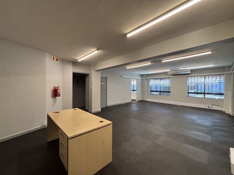 Spacious open-plan office area featuring tiled flooring, integrated air conditioning, and large windows with security bars for natural light.