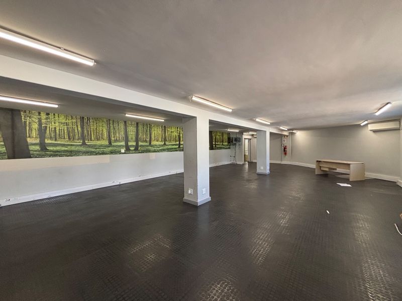 Spacious open-plan office area featuring durable rubber flooring, structural support columns, and integrated fluorescent lighting, suitable for a versatile workspace layout.