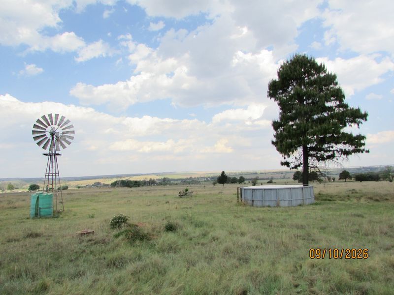 Expansive farm landscape featuring a traditional windmill, water storage tank, and reservoir set within open grazing land.
