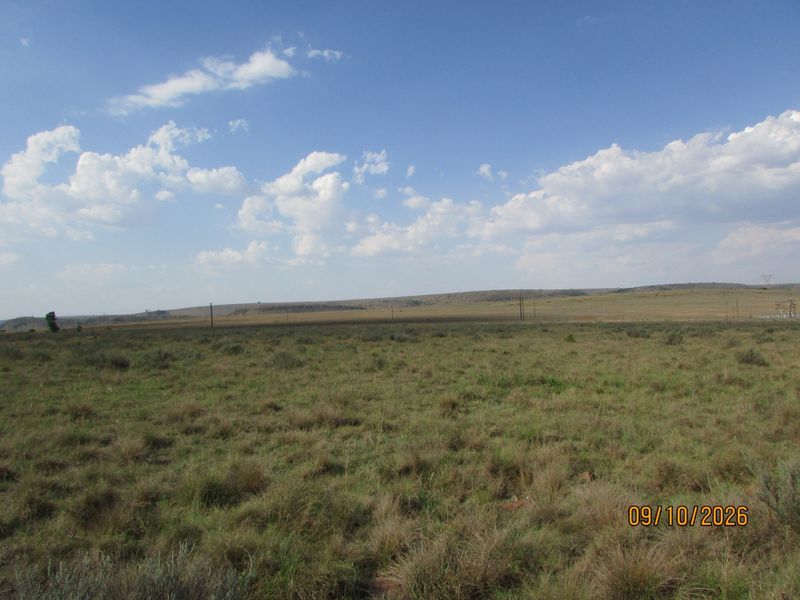 Expansive view of open farm land and natural grassland under a clear blue sky.