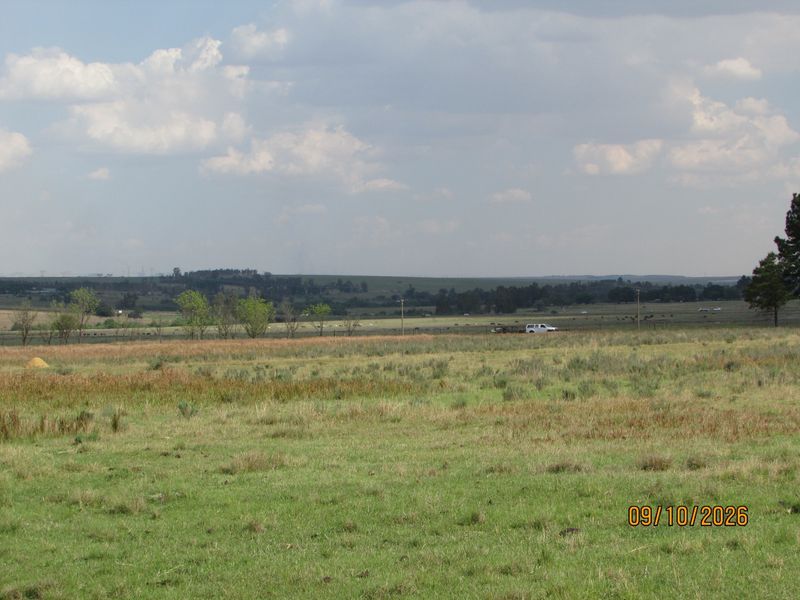 Expansive view of open farm pasture and rural landscape under a cloudy sky.
