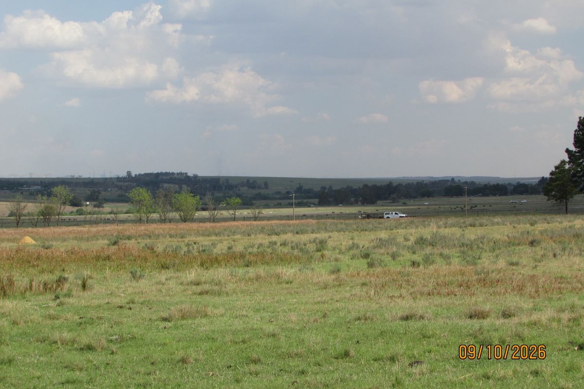 Expansive view of open farm pasture and rural landscape under a cloudy sky.