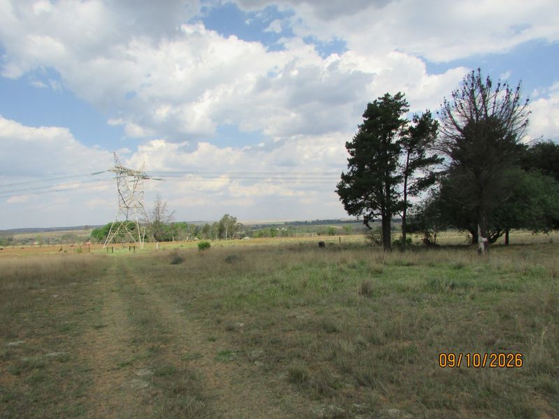 A wide landscape view of the farm property featuring open fields, mature trees, and visible high-voltage transmission infrastructure.