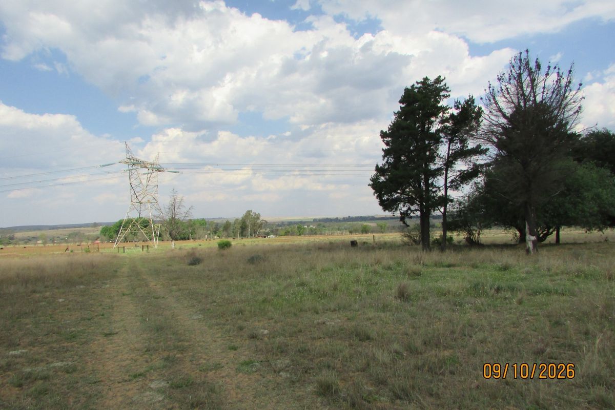 A wide landscape view of the farm property featuring open fields, mature trees, and visible high-voltage transmission infrastructure.