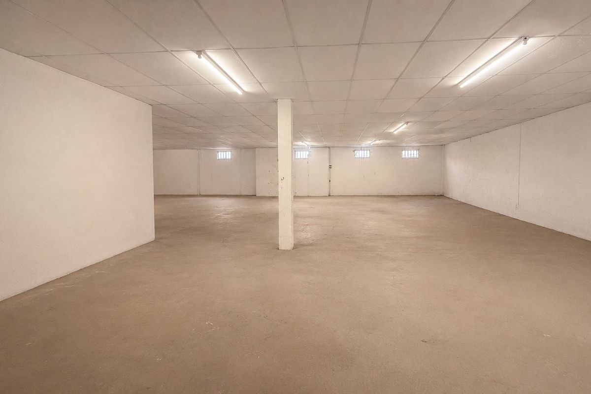 A large, open-plan commercial utility or storage space featuring concrete flooring, a suspended ceiling with fluorescent lighting, and small high-level windows.
