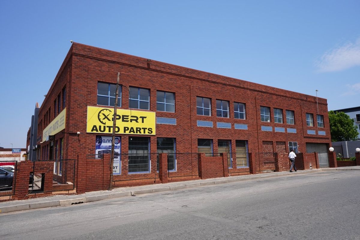 Commercial building featuring a prominent face brick facade, security fencing, and street-level access with roller shutter doors.