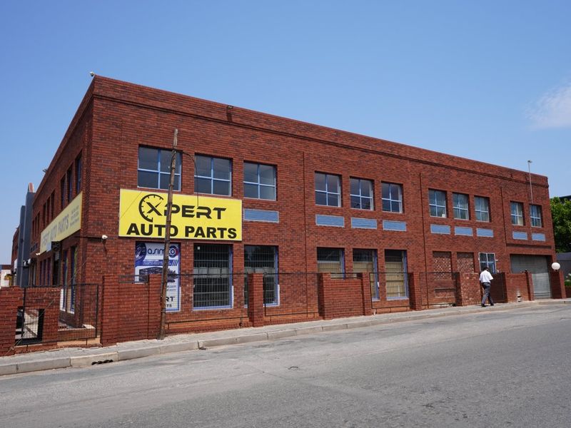 Commercial building featuring a prominent face brick facade, security fencing, and street-level access with roller shutter doors.