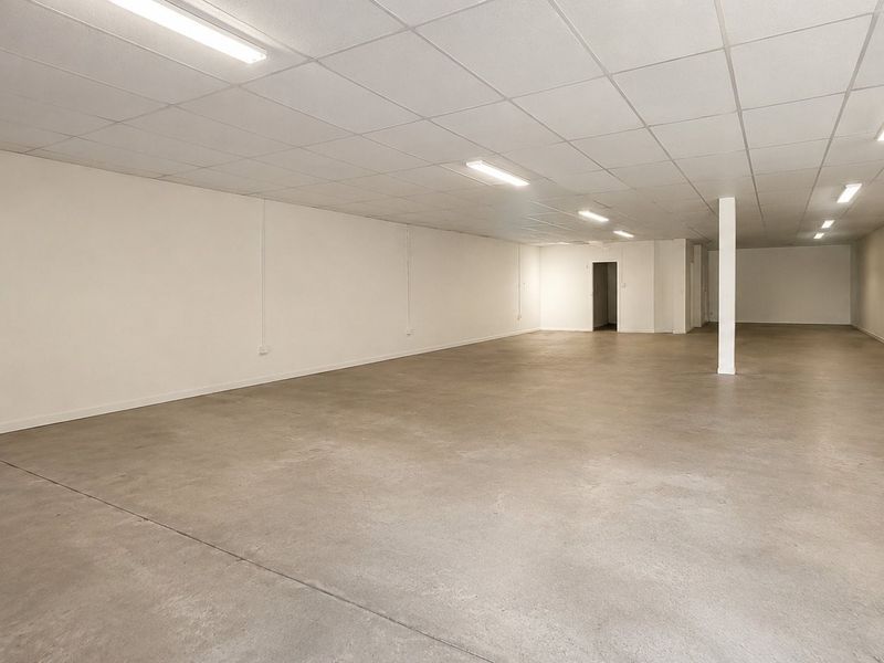 A spacious, open-plan commercial interior featuring a neutral finish, concrete flooring, and a suspended ceiling with integrated lighting, suitable for various business uses.