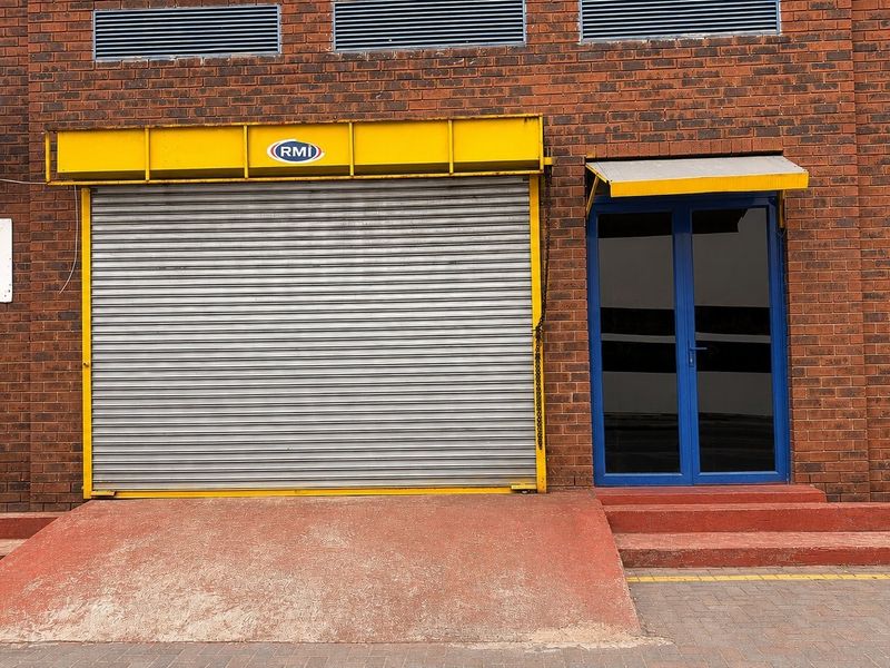 Commercial building exterior featuring a brick facade, a large roller shutter door with a loading ramp, and a glass entrance door.