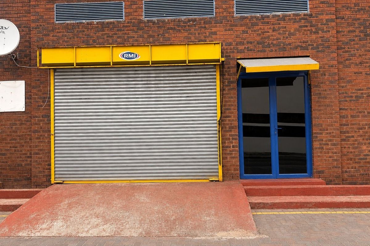 Commercial building exterior featuring a brick facade, a large roller shutter door with a loading ramp, and a glass entrance door.