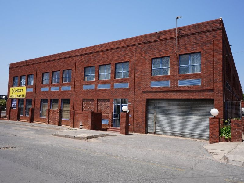 Commercial face brick building featuring a roller shutter door, security entrance, and multiple window bays, situated with direct street access.