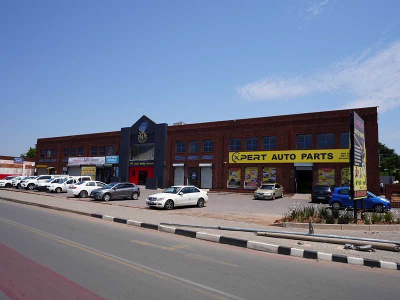 Front exterior view of a commercial brick building featuring multiple storefronts, security shutters, and an adjacent paved parking area.