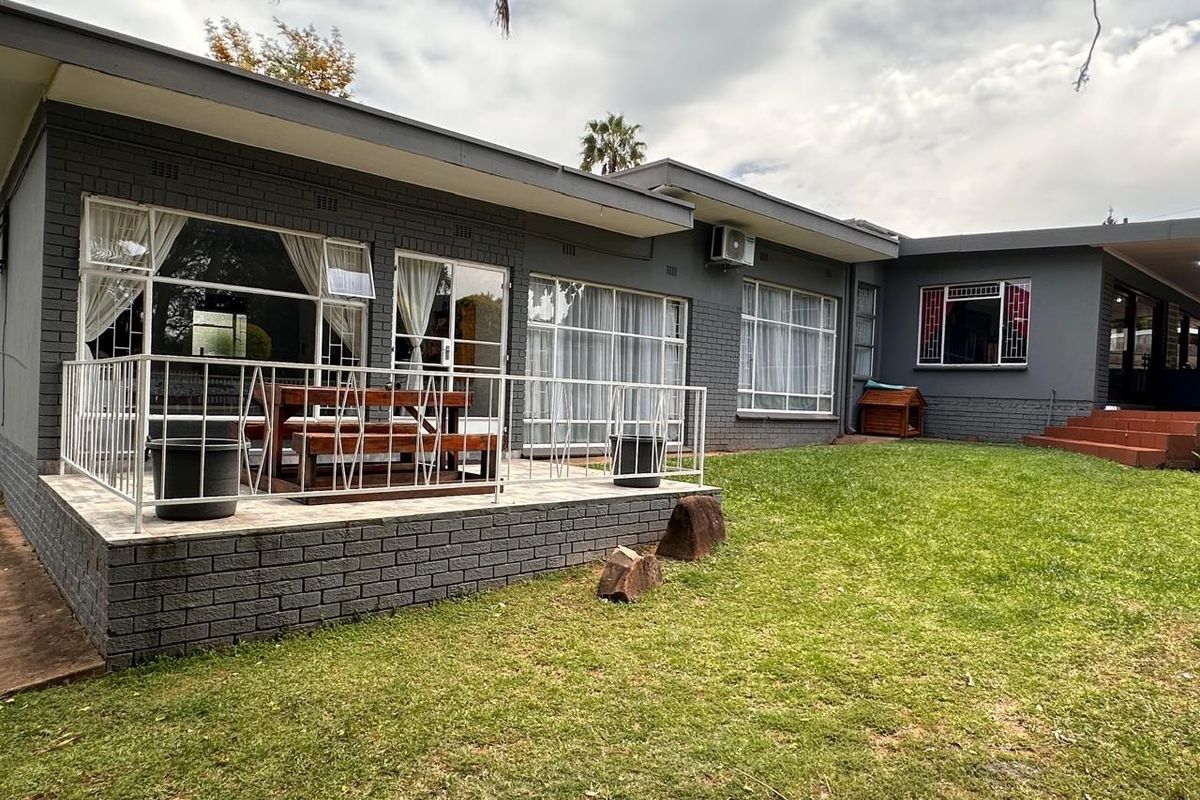 Rear view of the house featuring a paved patio area, brick exterior walls, large windows, and a well-maintained garden.