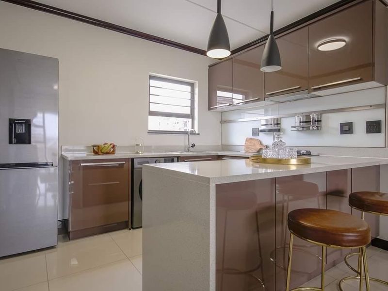 Modern kitchen featuring high-gloss cabinetry, quartz countertops, a breakfast bar, and sleek pendant lighting, offering a contemporary and functional culinary space.