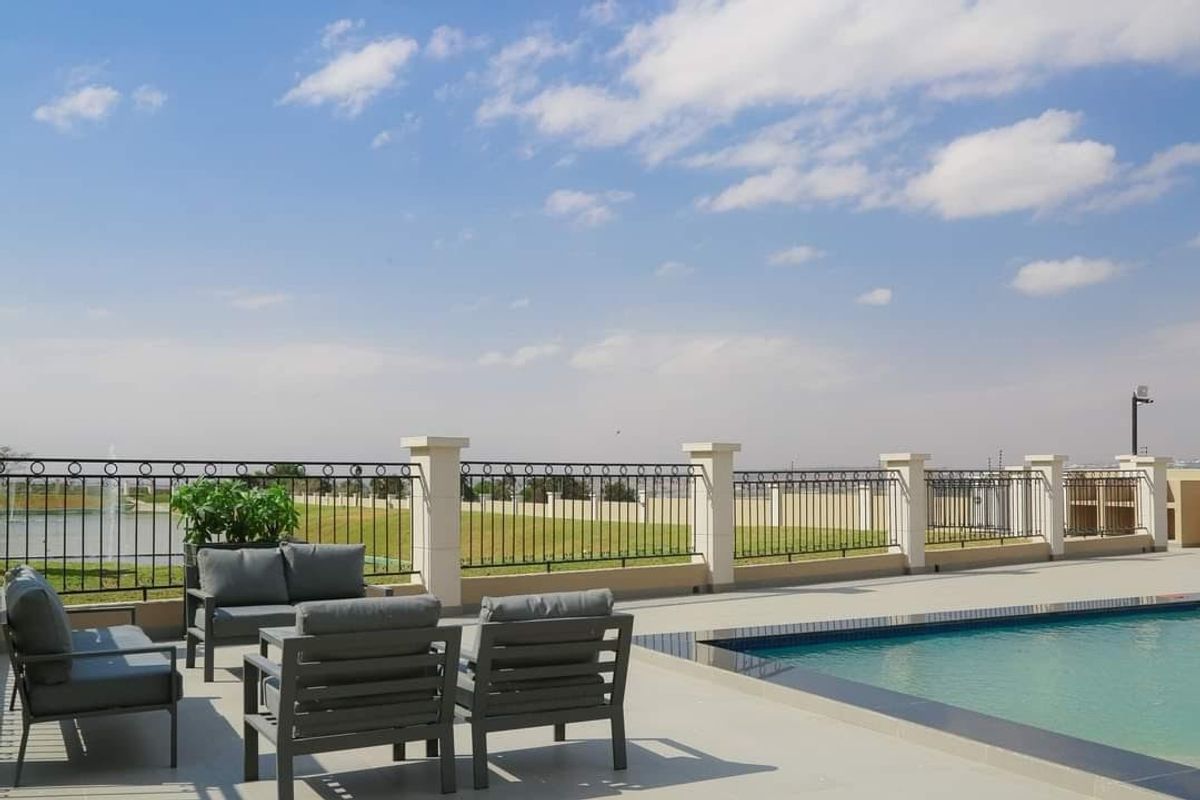 A well-maintained outdoor pool area featuring a paved deck, secure wrought iron fencing with masonry pillars, and clear views of the surrounding landscape.