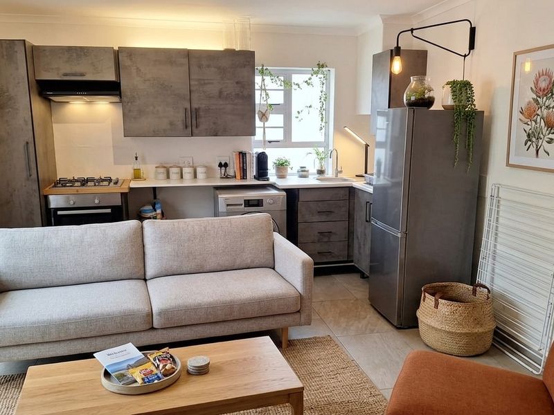 A modern open-plan living and kitchen area featuring contemporary grey cabinetry, integrated appliances, tiled flooring, and a functional layout.