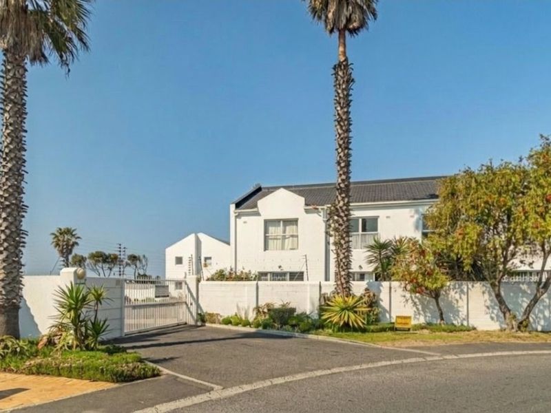 Front exterior view of the apartment complex featuring a secure gated entrance, paved driveway, and perimeter boundary wall with electric fencing.