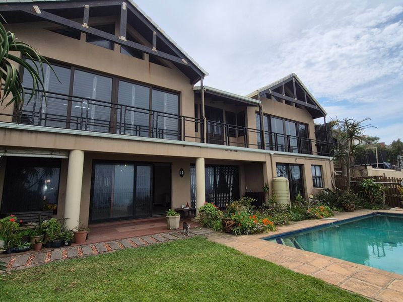Rear view of a double-story house featuring a swimming pool, paved patio area, upper-level balcony, and exposed timber roof trusses.