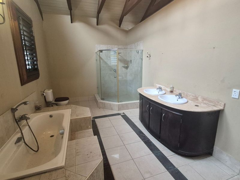 Spacious bathroom featuring a double vanity, built-in bathtub, glass shower enclosure, and vaulted ceilings with exposed timber beams.