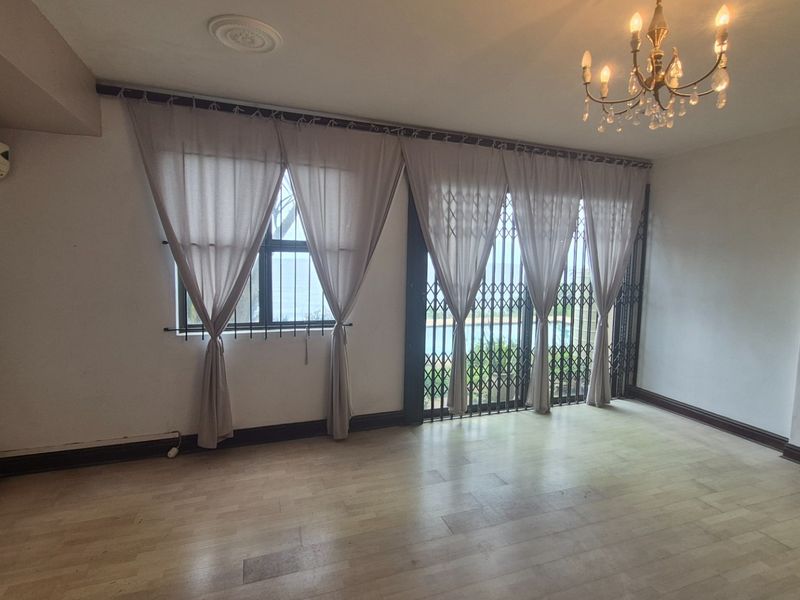 Spacious living area featuring laminate flooring, a split-system air conditioner, and security gates leading to an outdoor area.
