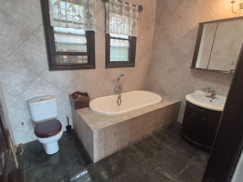 A functional bathroom featuring a built-in bathtub, vanity cabinet with basin, and tiled finishes throughout.