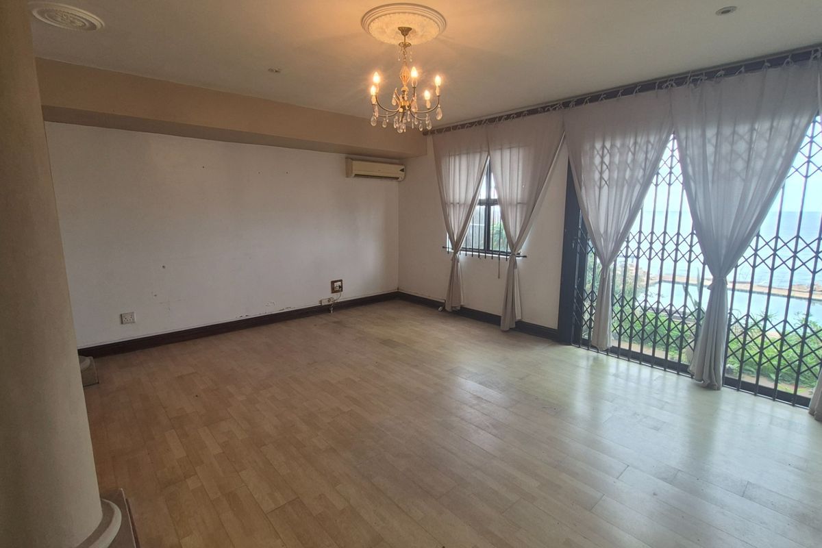 Spacious living area featuring laminate flooring, a decorative chandelier, and large sliding doors leading to an outdoor view with security gates.