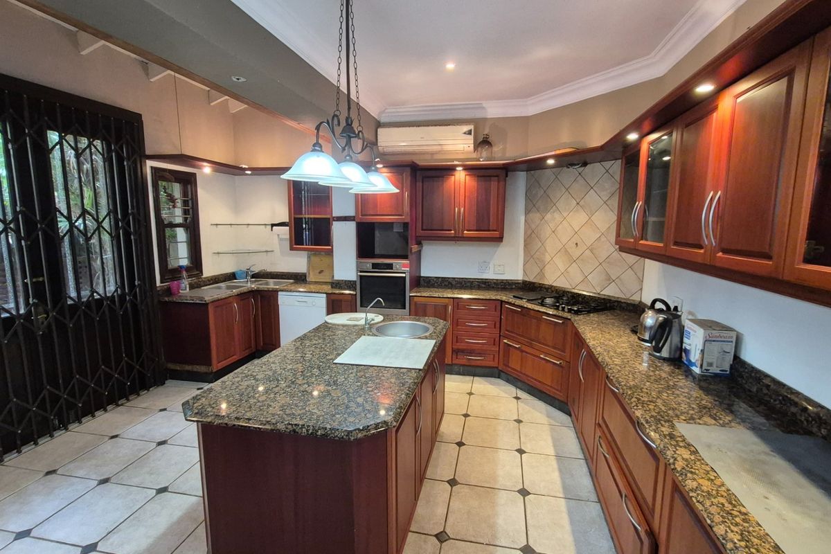 Spacious kitchen featuring dark wood cabinetry, granite countertops, a central island, built-in oven, gas hob, and tiled flooring with direct access to the exterior.
