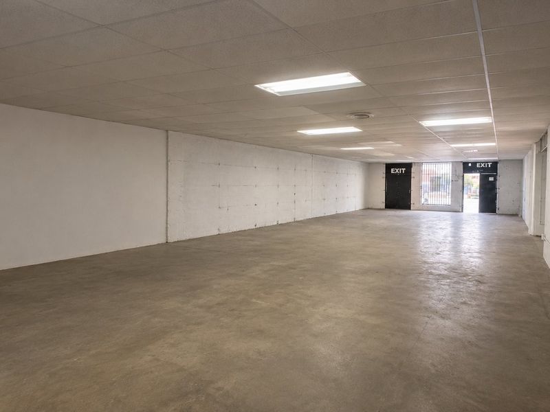 A spacious, open-plan commercial utility area featuring concrete flooring, a suspended ceiling with recessed lighting, and secure exit access.