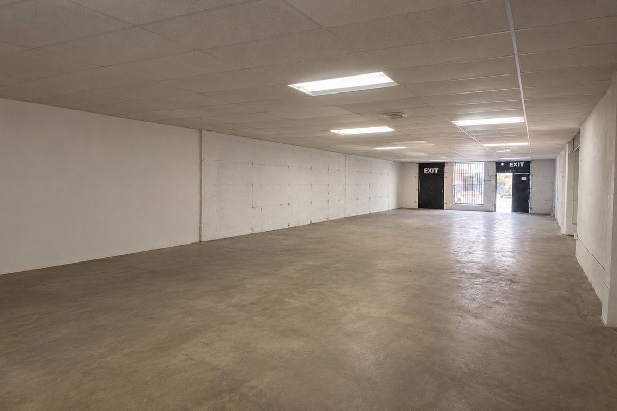 A spacious, open-plan commercial utility area featuring concrete flooring, a suspended ceiling with recessed lighting, and secure exit access.