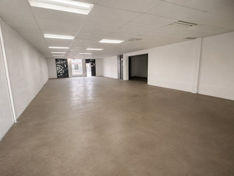 A spacious, vacant open-plan commercial unit featuring a suspended ceiling with recessed lighting and durable concrete flooring, suitable for various retail or office configurations.