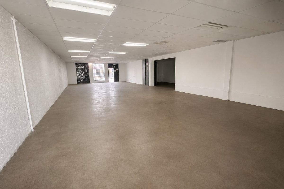 A spacious, vacant open-plan commercial unit featuring a suspended ceiling with recessed lighting and durable concrete flooring, suitable for various retail or office configurations.