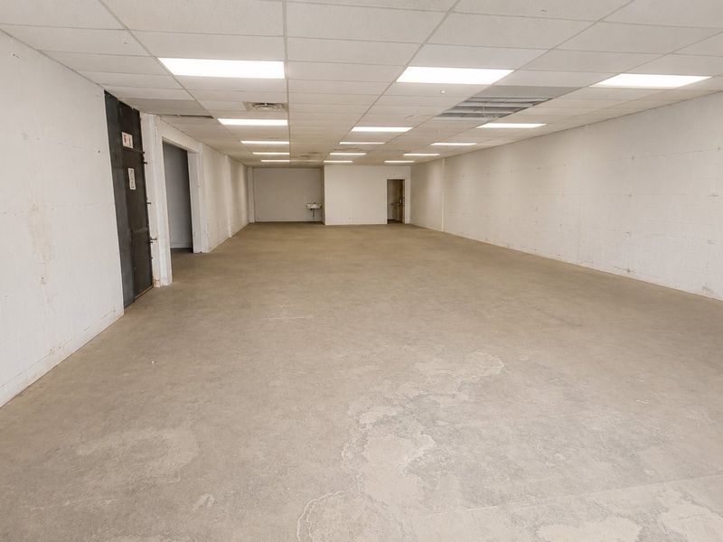 A large, open-plan commercial space featuring concrete flooring, exposed blockwork walls, and a suspended ceiling with recessed lighting.