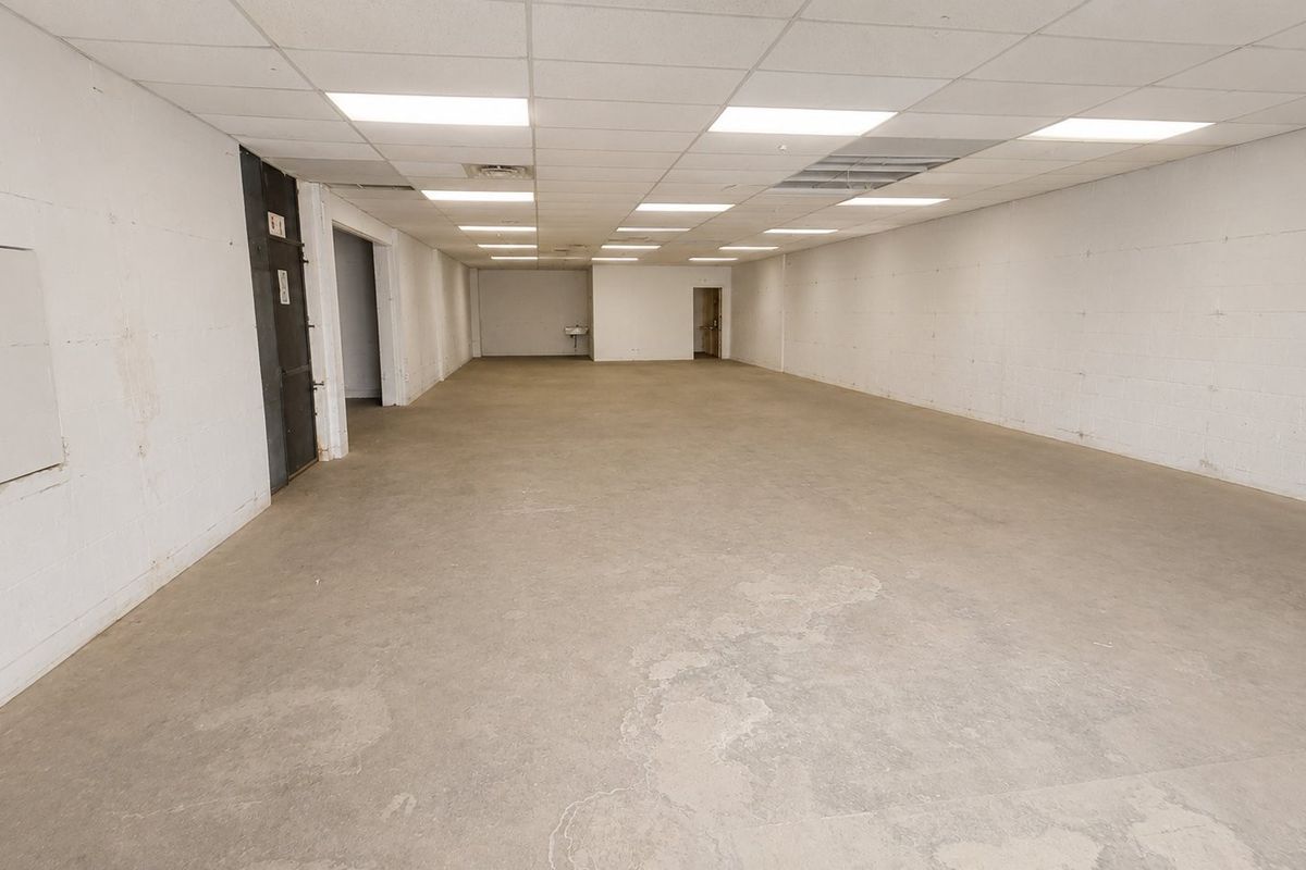 A large, open-plan commercial space featuring concrete flooring, exposed blockwork walls, and a suspended ceiling with recessed lighting.