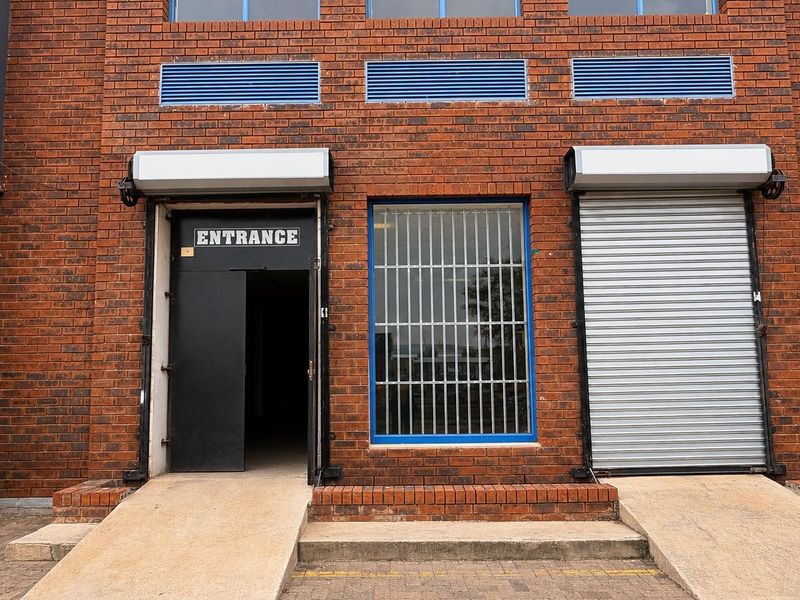 Commercial building entrance featuring a brick facade, security roller shutters, protective window bars, and concrete access ramps for improved accessibility.