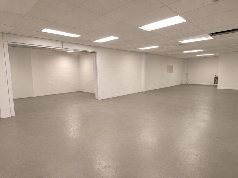 A spacious, open-plan commercial interior featuring durable epoxy flooring, painted brick walls, and a suspended ceiling with recessed lighting.