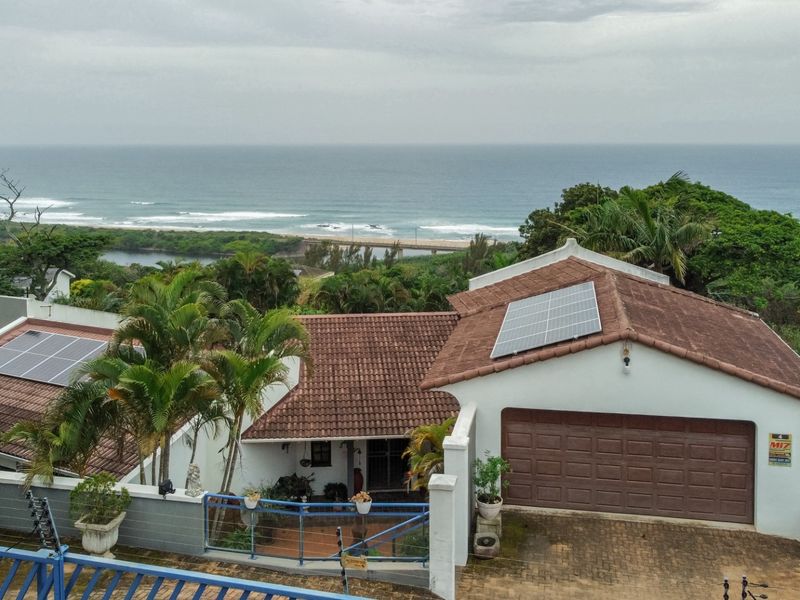 Aerial view of the property featuring a tiled roof with solar panels, a garage, and a scenic coastal outlook.
