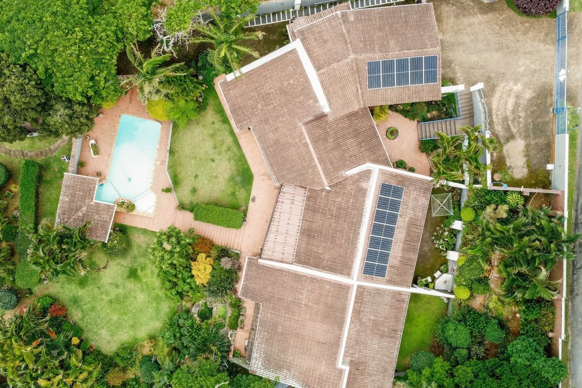 Aerial view of the property featuring a tiled roof with solar panels, a swimming pool, paved patio areas, and established garden landscaping.