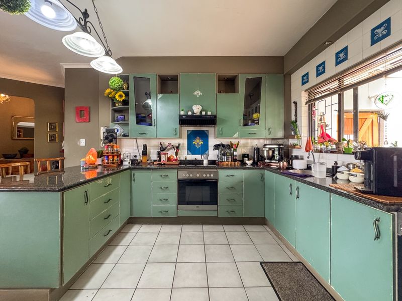 A U-shaped kitchen featuring green cabinetry, granite countertops, tiled flooring, and integrated appliances, offering a functional layout with ample storage space.