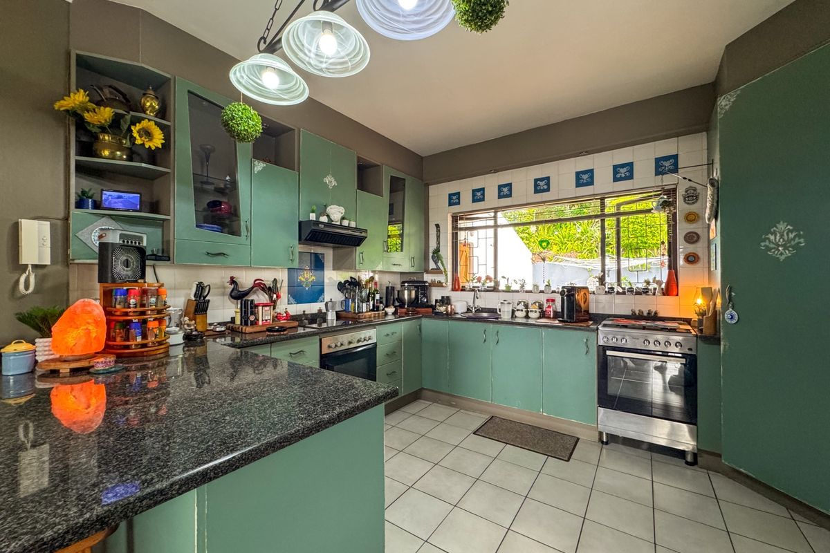 A functional kitchen featuring green cabinetry, granite countertops, a built-in oven, and a tiled backsplash with a window overlooking the garden.