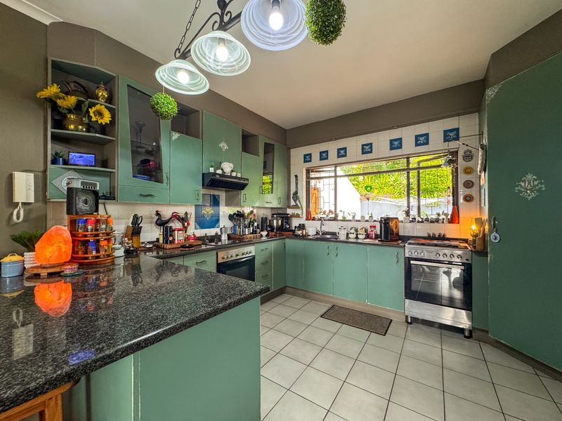 A functional kitchen featuring green cabinetry, granite countertops, a built-in oven, and a tiled backsplash with a window overlooking the garden.