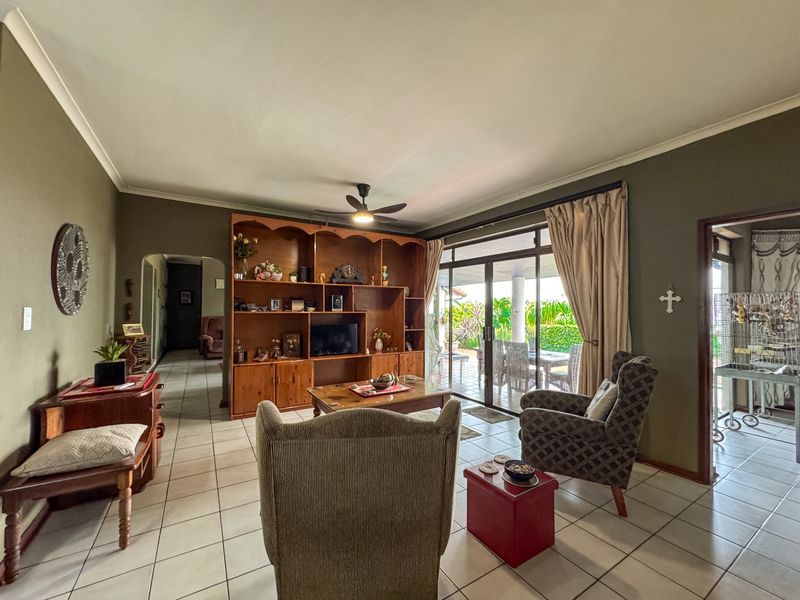 A spacious living room featuring tiled flooring, a large built-in wooden display unit, and sliding glass doors providing direct access to the patio.