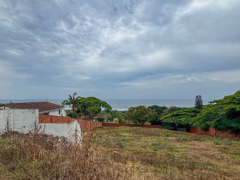 A vacant residential plot featuring an expansive ocean view, enclosed by brick boundary walls and surrounded by established coastal greenery.