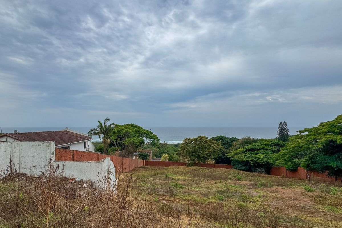 A vacant residential plot featuring an expansive ocean view, enclosed by brick boundary walls and surrounded by established coastal greenery.