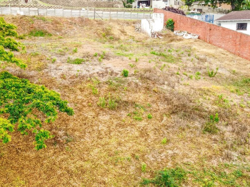 An elevated view of a vacant residential plot featuring a brick boundary wall and existing retaining structures, ready for development.