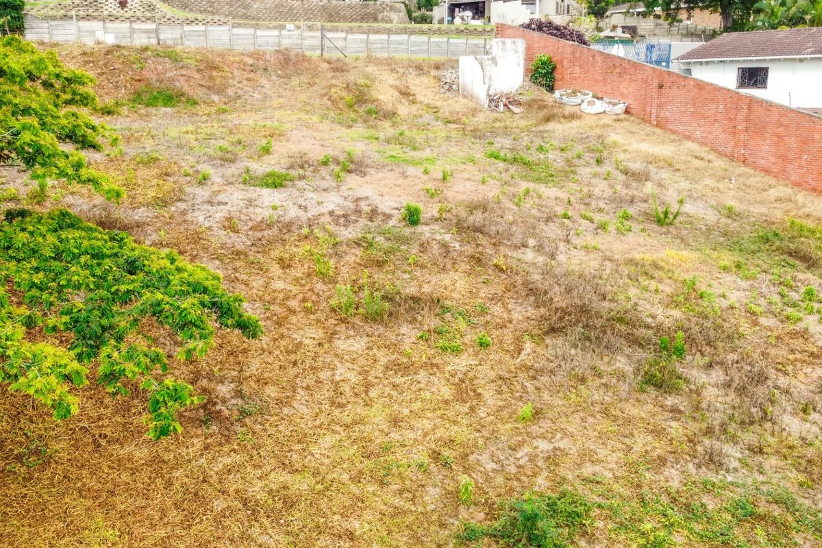 An elevated view of a vacant residential plot featuring a brick boundary wall and existing retaining structures, ready for development.