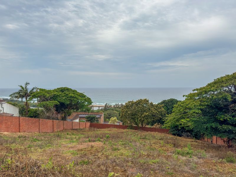A vacant residential plot featuring a brick boundary wall and an expansive view of the ocean and surrounding landscape.