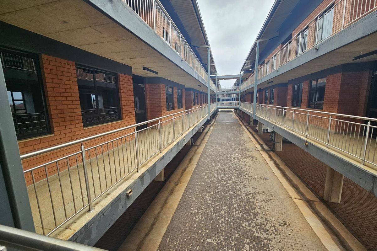 Exterior view of a multi-story office complex featuring brick facades, covered walkways with metal railings, and a central paved driveway.