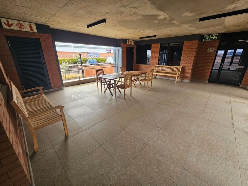 A covered outdoor patio area featuring face brick walls, tiled flooring, and an exposed concrete ceiling with emergency exit signage.